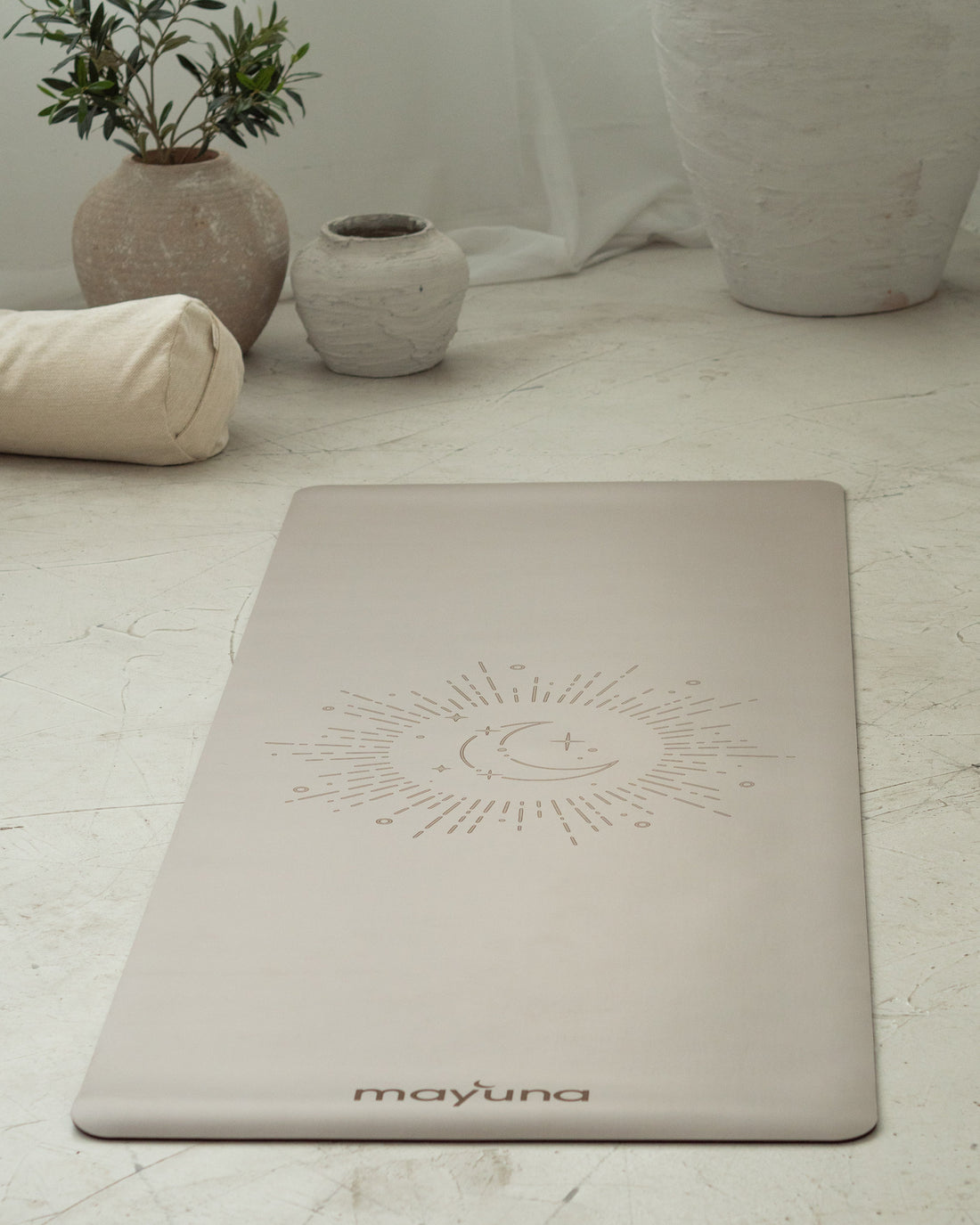 Mayuna Yogamatte in Mauve mit Sonne-Mond-Gravur, ausgerollt auf Steinboden, im Hintergrund Bolster und Keramikvasen