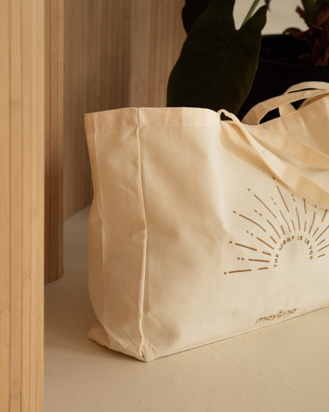 Mayuna Tasche The light is in you mit Sonnenstickerei auf einem Regal neben einer Pflanze