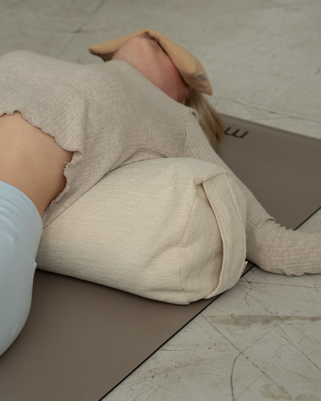 Frau liegt rücklings über dem Mayuna Yogabolster, das Lavendel Augenkissen liegt auf ihren Augen