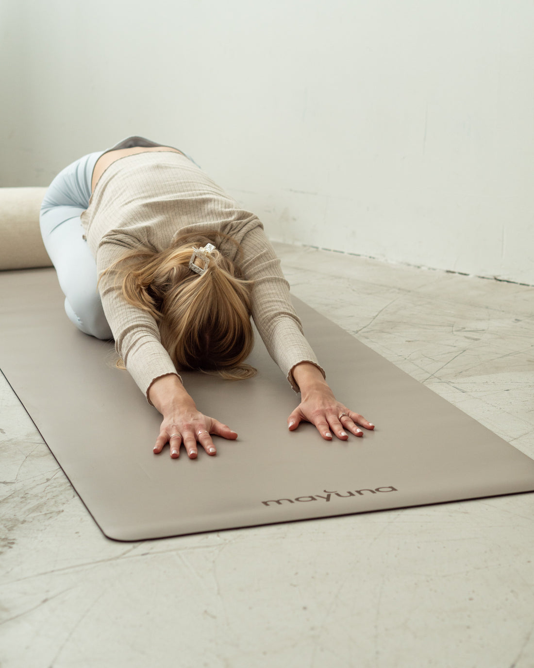 Frau in der Kindhaltung auf der Mayuna Yogamatte Natural in Taupe, daneben ein Yogabolster