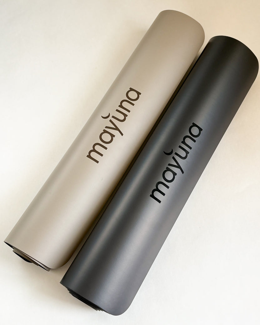 Zwei zusammengerollte Mayuna Yogamatten in Taupe und Schwarz mit Logo-Aufdruck