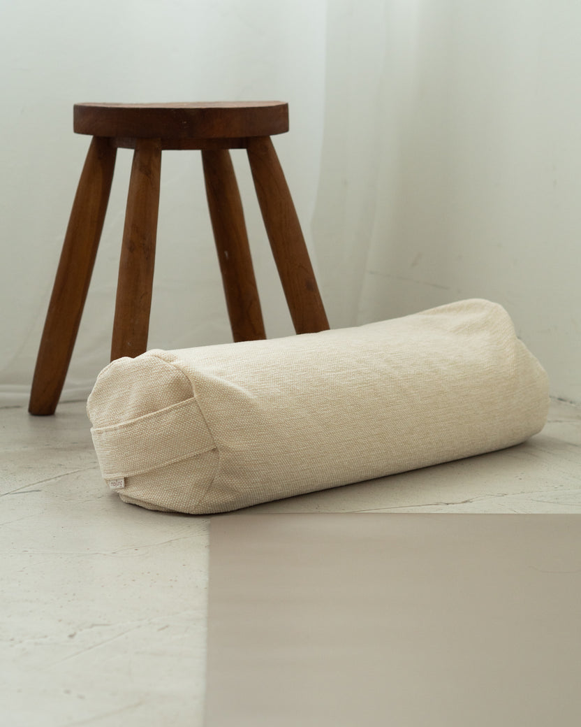 Mayuna Yogabolster in Sand auf Steinboden, im Hintergrund ein Hocker aus dunklem Holz